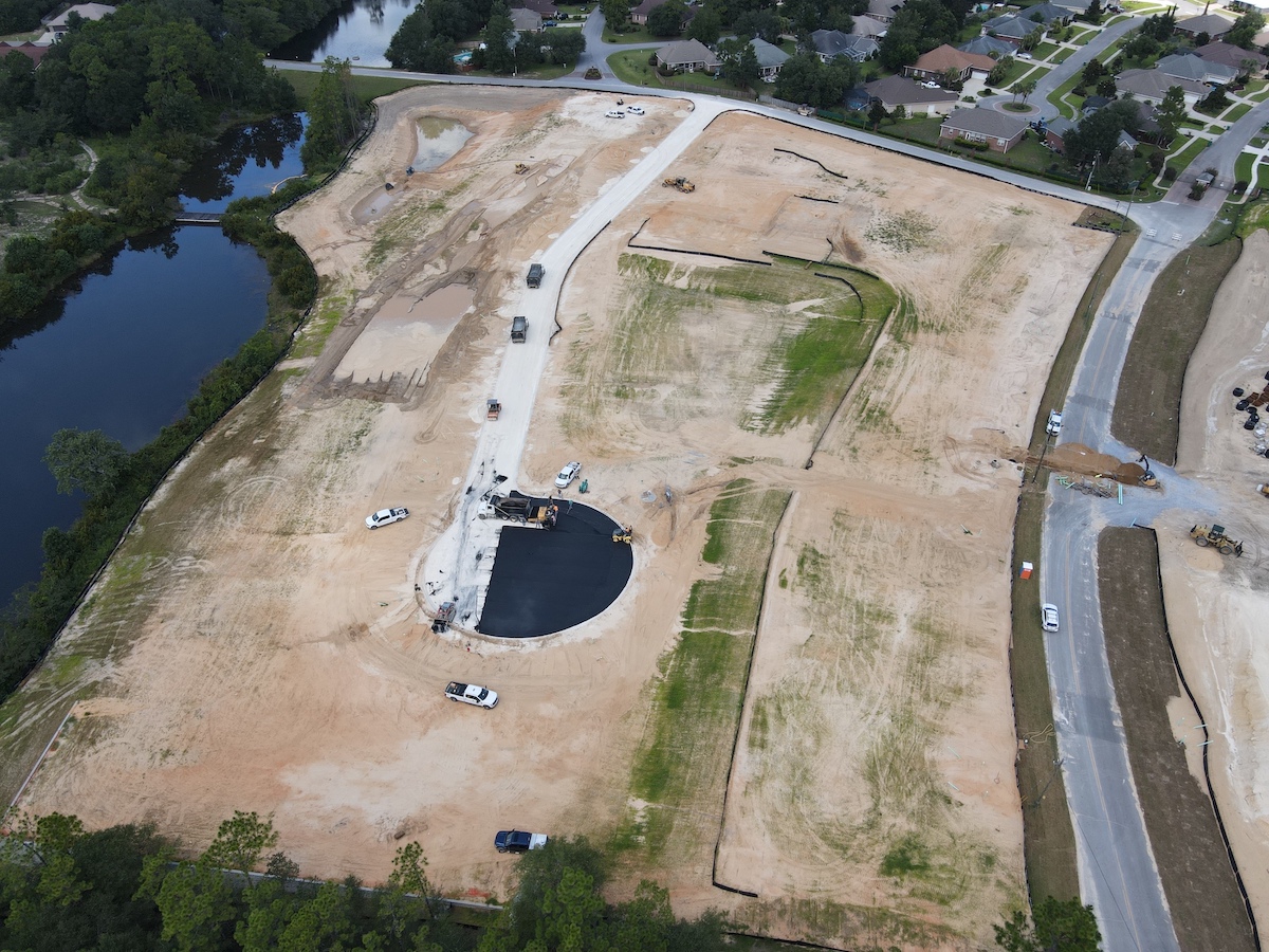Aerial image of a residential project in Crestview, FL shows Green Energy road building crews laying asphalt in a partially completed cul-de-sac. Bordering the job site are roads, a neighborhood, trees, and a pond